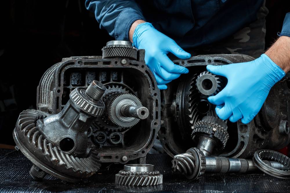 Engine & Transmission Services Hands of a male repairman in blue gloves on a background of a gearbox, close-up. Repair box predach, repair of used cars. Metal background.