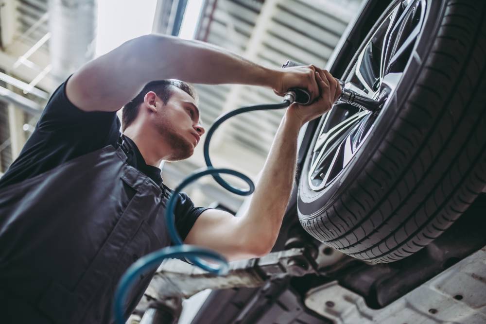 Tire Services Handsome mechanic in uniform is working in auto service. Car repair and maintenance. Twisting/untwisting bolts on wheel.